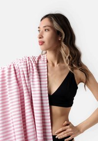 Asciugamano rigato rosa e bianco appoggiato sulla spalla, realizzato in materiale morbido. Modella indossa un top bikini nero. Design semplice e pulito con una texture leggera.