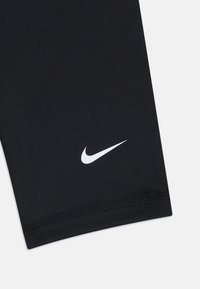 Čierne športové legíny vyrobené z elastického materiálu, s bielym logom Nike blízko lemu a hladkou, nezdobenou textúrou.