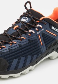 Pantofii de alergare pe traseu pentru bărbați au un superior de culoare albastru marin, accente portocalii, material texturat GORE-TEX și o talpă exterioară albă robustă.