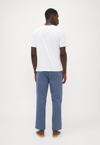 Hvid t-shirt med korte ærmer og blå stribede pyjamasbukser. Bukserne har lige pasform og har lodrette striber i varierede bredder.