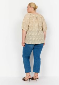 Top beige con occhioletto e maniche ampie, abbinato a jeans blu dritti e tacchi in stampa leopardata. Vestibilità ampia e dettagli in tessuto testurizzato.