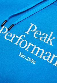 Felpa con cappuccio in tessuto blu brillante, con il testo ricamato bianco "Peak Performance" e "Est. 1986", dalla superficie strutturata.