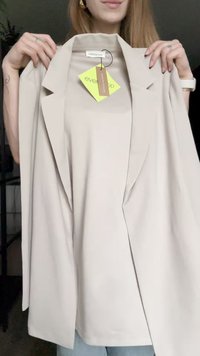 Beige blazer med strukturerte skuldre, åpen frontdesign og glatt stoff. Tag festet med merkevarenavn og vedlikeholdsinstruksjoner synlig.