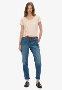 Beige kortærmet t-shirt parret med lyseblå, højtaljede jeans. En brun vævet bælte, sorte loafers og cremede sokker fuldender outfittet.