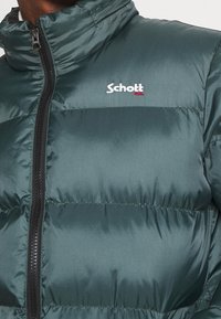 Uomo che indossa un giubbotto imbottito verde scuro con zip nera e il logo bianco "Schott NYC" sul petto.