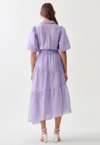 Lavender tiered maxi dress with puff sleeves and a tied waist, made of lightweight fabric, featuring a layered hem that flows gently.
