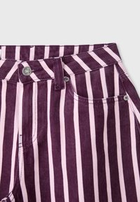 Gros plan d’un pantalon à rayures verticales violettes et rose clair avec un bouton, une boucle de ceinture et une poche avant.