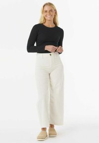 Sort langærmet top parret med høj talje og vidde hvide bukser. Bemærkelsesværdige detaljer inkluderer en knap i taljen og beige slip-on fodtøj.