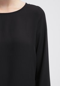 Svart långärmad topp med rund halsringning, tillverkad av ett slätt, lätt material. Har minimala sömmar för ett elegant utseende.