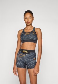 Conjunto de top deportivo y pantalones cortos de UFC en un patrón de camuflaje negro y gris, con un diseño ajustado y acentos naranjas en contraste.