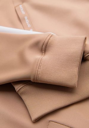 Lichtbruin sportstof met een getextureerde mouwboord met een gladde afwerking, voorzien van een witte accenta en een logo-label.