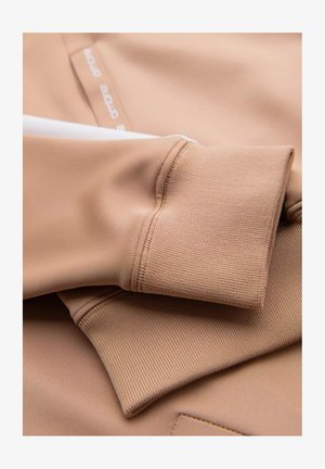 Lichtbruin sportstof met een getextureerde mouwboord met een gladde afwerking, voorzien van een witte accenta en een logo-label.