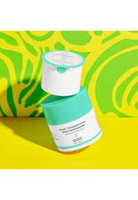 A teal and white jar of Protini Polypeptide Cream with a peel-off lid, featuring text labels and a vibrant yellow-green abstract background.