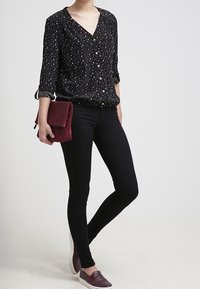 Černá košile na knoflíky s bílými skvrnami, zkombinována s černými skinny džíny a burgundskou kabelkou; modelka má na sobě šedé slipped-on boty.