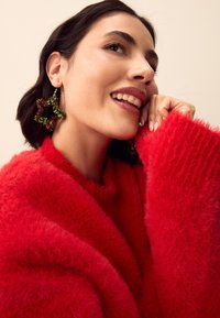 Red fuzzy sweater with long sleeves, featuring green and red star-shaped earrings. Close-up of the neck area with a soft texture.