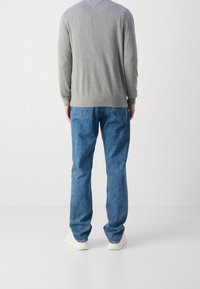 Grauer Strickpullover mit gerippten Bündchen, kombiniert mit blauen Denim-Jeans mit geradem Bein und Gesäßtaschen, getragen mit hellen Schuhen.