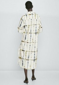 Pitkä, löysä tunikamekko kermansävyisestä kankaasta, jossa on oliivin, sinisen ja ruskean sävyinen tye-dye-kuvio. Sisältää kauluksen ja napit.