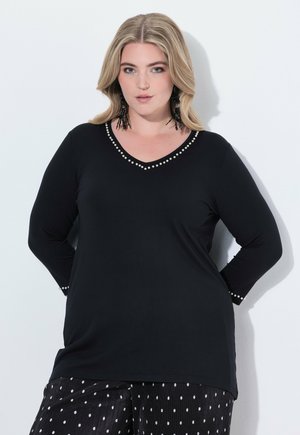 Schwarzes Langarmshirt mit V-Ausschnitt und Perlenakzenten entlang des Ausschnitts. Weicher Stoff, kombiniert mit einer Hose in Schwarz-Weiß mit Punkten.