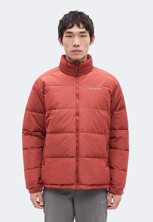 Mann trägt rostfarbene gesteppte Columbia-Jacke mit durchgehendem Frontreißverschluss und Stehkragen, kombiniert mit grauer Hose.