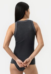 Donkergrijze geribde tanktop met kantafwerking op de schouders, met een aangesloten ontwerp. Model is gezien vanuit de rug, met de handen gekruist achter.