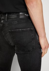 Jeans in denim nero con una vestibilità slim, dotati di una tasca posteriore con un design a cucitura curva e di un'etichetta in pelle nera con il marchio sulla vita.