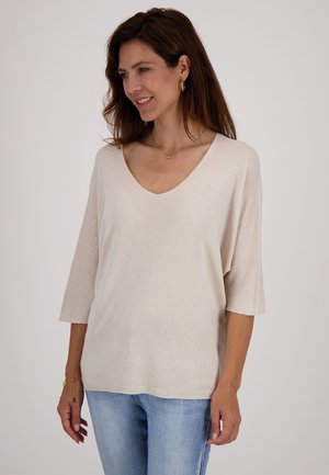 Beige V-hals trui met 3/4 mouwen, gemaakt van zachte textuurstof; gecombineerd met licht gewassen jeans, die een ontspannen pasvorm en casual stijl tonen.