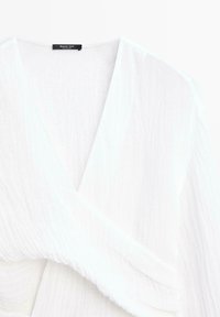 Weiße, geknitterte Stoffbluse mit tiefem V-Ausschnitt und geraffter Taille, mit einem "Massimo Dutti"-Etikett im inneren Kragen.