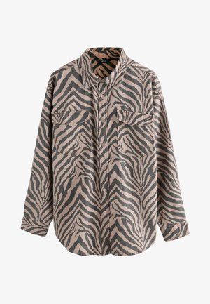 Vrouw die een bijpassend oversized jasje en korte broek met zebraprint draagt, gecombineerd met een zwart topje, staand buiten op een houten terras.