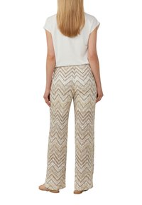 Losse, hooggewaiste broek met een zigzagpatroon in beige en wit, gemaakt van een gestructureerd geweven materiaal. Gestyled met een basic witte top.