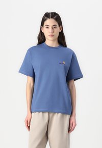 Blaues Baumwoll-T-Shirt mit Rundhals und kurzen Ärmeln. Verfügt über ein kleines gesticktes Logo in Gelb und Burgunder auf der linken Brust.
