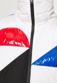 Padded jacket featuring a white base, gloss red, blue, and black geometric shapes, front zipper, and high collar design.