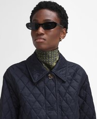 Navy quilted jacket with large collar and button closure, paired with a green polka dot scarf and black oval sunglasses.