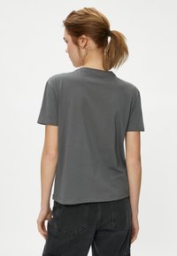 T-shirt en coton gris à manches courtes, col rond et ourlet tombant légèrement en dessous de la taille. Design simple sans motifs visibles.