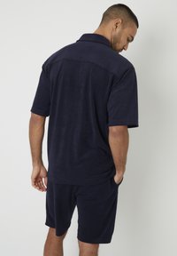 Polo a maniche corte blu navy realizzato in materiale morbido, caratterizzato da una vestibilità rilassata, colletto e tasca sui pantaloni.