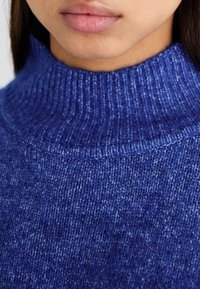 Maglione blu a maglia con colletto alto e a coste. La texture appare morbida con un sottile motivo mélange in diverse sfumature di blu.