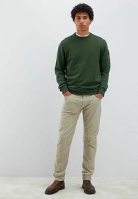 Maglione verde con collo rotondo e polsini a coste, abbinato a pantaloni beige chiaro e stivali in pelle marrone. Design semplice e casual senza pattern.
