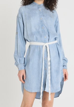 Vestido camisa de mezclilla azul claro de manga larga con botones al frente, dobladillo asimétrico y cinturón trenzado blanco atado a la cintura.