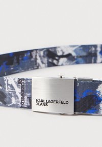 Καμβάς ζώνη σε μπλε και μαύρο με αφηρημένα σχέδια. Διαθέτει ασημί μέταλλο κούμπωμα με την επωνυμία "KARL LAGERFELD JEANS".