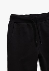 Sorte sweatpants lavet af blødt stof med elastisk taljebånd og sidelommer. Renset design og glat tekstur.