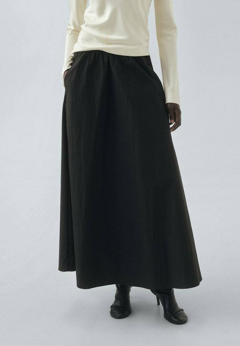 Schwarzer Maxikleid aus strukturiertem Stoff, mit einem gerafften Bund und einer fließenden Silhouette, kombiniert mit schwarzen Absatzstiefeln.