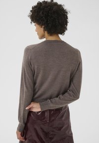 Brown knitted sweater with long sleeves, a round neck, and ribbed cuffs. The fabric appears soft, paired with a glossy burgundy skirt.