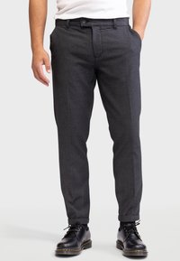 Pantalons en tissu texturé gris avec une coupe slim, dotés d'une fermeture à bouton devant et de poches latérales, associés à des chaussures noires.