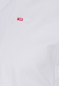 T-shirt bianco in cotone con un piccolo logo "Diesel" rosso e bianco sul lato superiore sinistro. Tessuto morbido con un classico scollo rotondo.