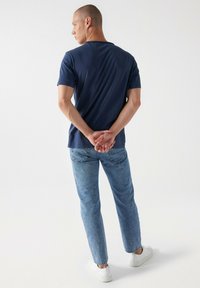 Námořnické tričko s krátkým rukávem v kombinaci se světle modrými džíny. Džíny mají odřené praní a klasický design s pěti kapsami, doplněné bílými teniskami.