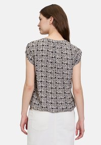 Kortebloemige blouse in zwart en crème met een geometrisch bladdessin. Zachte stof, ontspannen pasvorm, met subtiele plooien langs de achterkant van de halslijn.