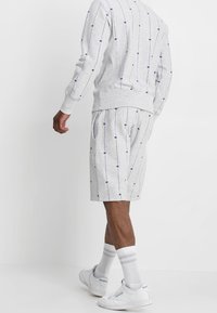 Lichtgrijze sweatshirt en bijpassende shorts met verticale strepen en kleine paarse accenten. Gemaakt van textuurstof; strakke pasvorm.