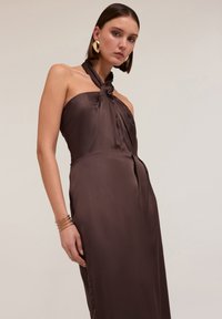 Rochie halter din satin maro, cu un gât legat și o siluetă ajustată, având o textură netedă și detalii pe cusătura laterală.