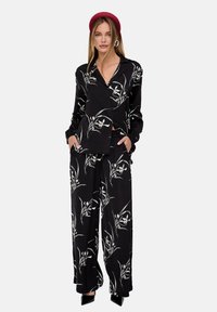 Black silk pajama set with floral pattern, featuring a long-sleeve button-up shirt and wide-leg pants with pockets. Hat and earrings as accessories.