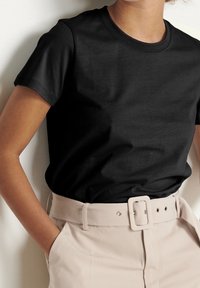 Sort bomuld T-shirt med korte ærmer og rund hals, kombineret med beige bukser med bredt bælte og spænde-detalje.