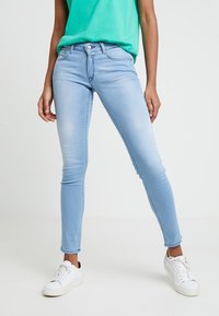 Jeans skinny de color azul claro fabricados en denim, con un diseño clásico de cuatro bolsillos, cierre de cremallera y un acabado ligeramente desgastado. Combinados con zapatillas blancas.